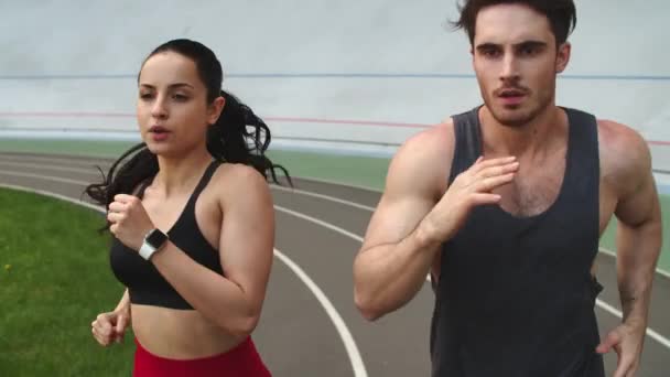 Portrait of sporty couple running at sport stadium. Fit man and woman sprinting — Stockvideo