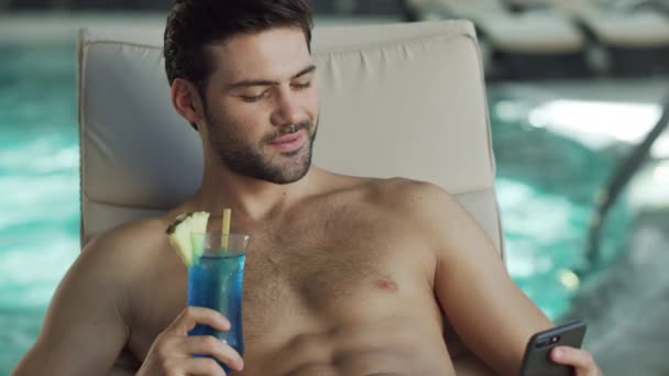 Крупный план сексуальный мужчина расслабляется с телефоном у бассейна. Веселый человек прокручивает мобильный — стоковое видео