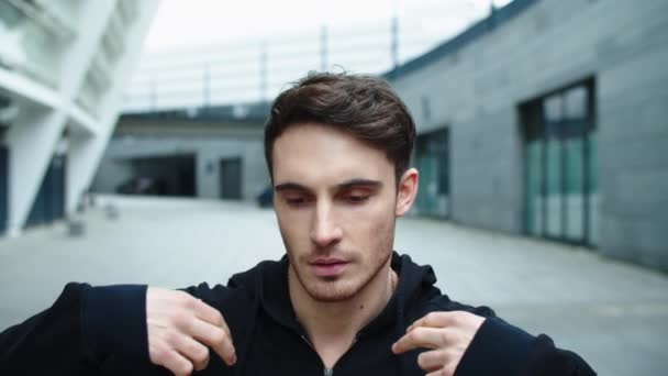 Portrait of handsome man walking street. Close up focused guy correcting hood — Stockvideo