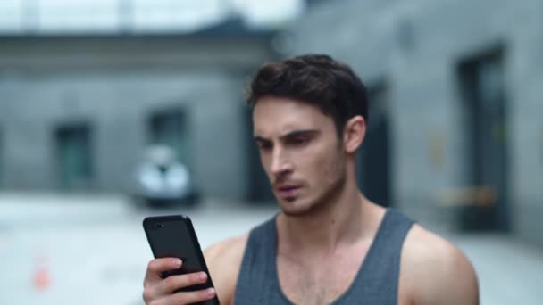 Close-up atleet man op zoek smartphone op straat. Glimlachende man leest bericht — Stockvideo