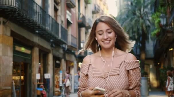 Mulher feliz andando em fones de ouvido em câmera lenta. Menina bonito flertando ao ar livre. — Vídeo de Stock