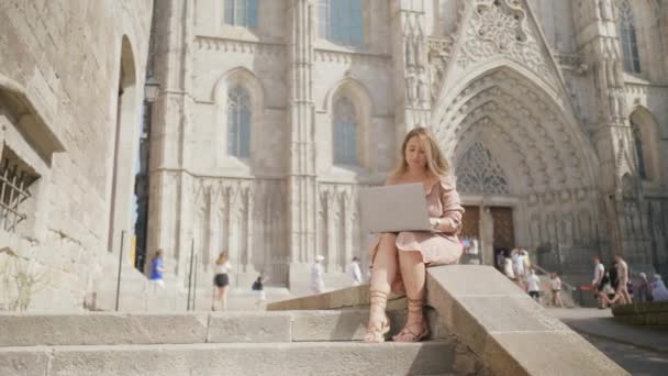 Lachende vrouw die werkt met een laptop in de buurt van de kathedraal. Glimlachend meisje krijgt bericht — Stockvideo