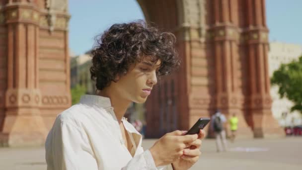 Портрет молодого чоловіка, який дивиться мобільний телефон на вулиці. Орієнтований хлопець за допомогою смартфона — стокове відео