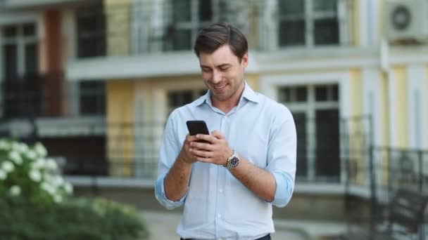 Uomo felice che digita al telefono all'aperto. Uomo che scrive un messaggio al telefono in strada — Video Stock