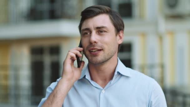 Закрыть бизнес говорящий телефон. Мужчина разговаривает по телефону в рубашке на улице — стоковое видео
