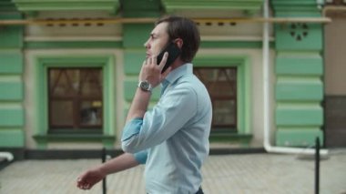 Ciddi bir iş adamı dışarıda telefonla konuşuyor. İş adamı akıllı telefonuyla yürüyor