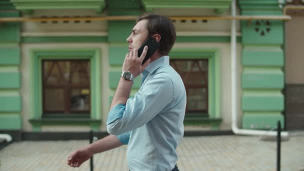 Серьезный бизнесмен разговаривает по телефону на улице. Бизнесмен ходит со смартфоном — стоковое видео