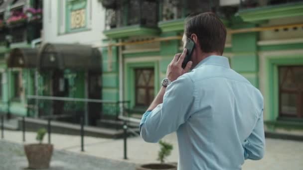 Bakåt bild av affärsman promenader med mobiltelefon på city street — Stockvideo