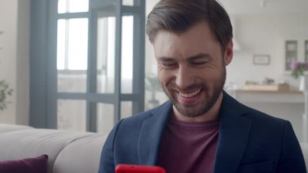 Schöner Geschäftsmann, der zu Hause mit dem Handy lacht. Kerl liest lustigen Text. — Stockvideo
