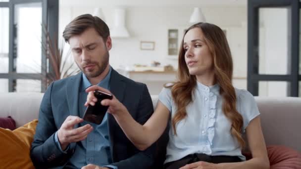 Verveelde vrouw die thuis de telefoon van een man meeneemt. Verveeld koppel zittend op de bank. — Stockvideo