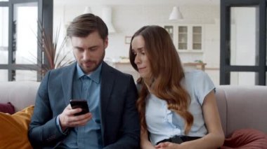 İş çifti kanepede birlikte dinleniyor. Sinirli kadın erkek telefonuna bakıyor.