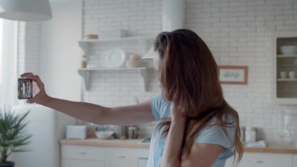 Vrolijke vrouw knipoogt naar telefoon camera in de keuken. Meisje neemt selfie foto. — Stockvideo