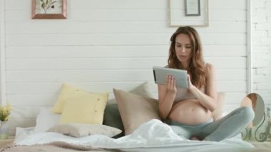 Pregnant belly woman watching tablet bed. Expectant mother surfing internet home