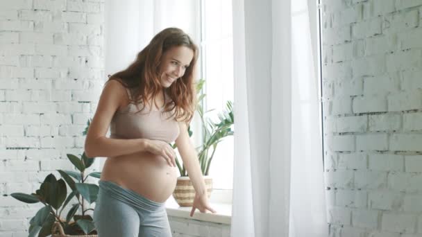 Closeup pregnant woman touching belly. Expecting mother standing window at home. — Stok video