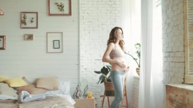 Pregnant woman touching belly near window at home. Smiling belly mother at home.