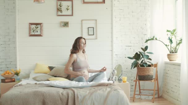 Gezonde zwangere vrouw die yoga beoefent in bed. Zwangere mediteren binnen. — Stockvideo