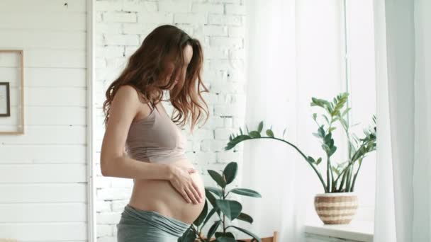 Pregnant standing bedroom window. Expecting belly mother stroking belly at home. — Stok video