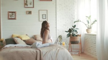 Pregnant woman getting up in bedroom. Expectant mother stroking belly at home