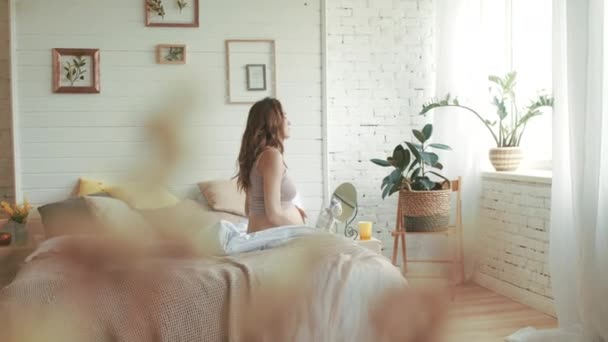 Беременная женщина встает в спальне. Ожидаемая мать гладит живот дома — стоковое видео