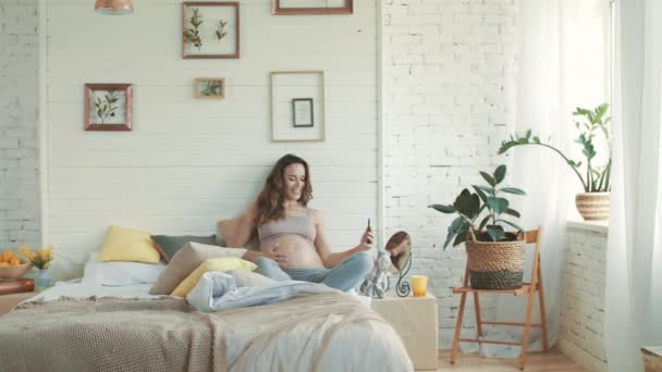 Smiling pregnant woman taking selfie photo at home. Belly mother sitting in bed. — Stockvideo