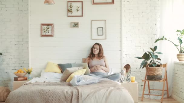 Mujer embarazada trabajando portátil en casa. Alegre vientre madre sentado cama . — Vídeo de stock