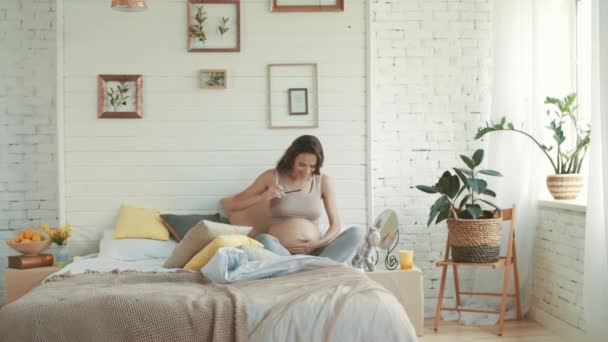 Jovem grávida tomando selfie da barriga em casa. Feliz barriga mãe sentado cama — Vídeo de Stock