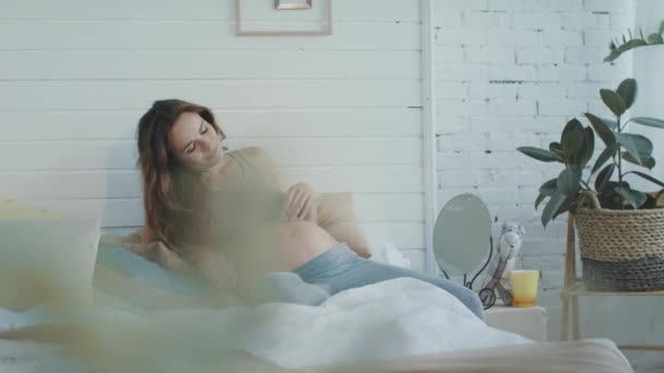 Mooie zwangere vrouw die haar buik aanraakt. buik moeder liggend op bed kussens — Stockvideo