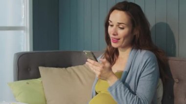 Macro laugh pregnant woman looking on smartphone screen in modern living room.