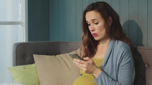 Schwangere berührt Handy-Bildschirm auf Couch zu Hause. — Stockvideo