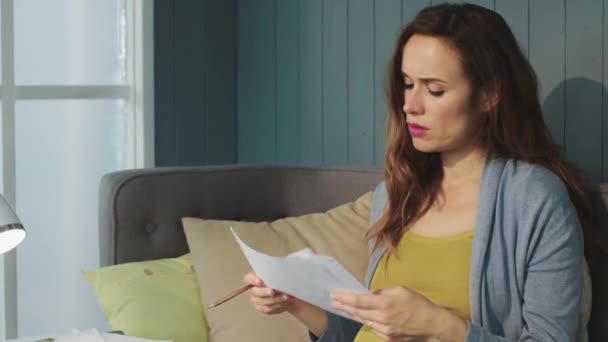 Macro serious pregnant woman working with papers on couch in living room. — Stock Video