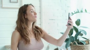 Macro beautiful pregnant woman taking selfie photo in bright bedroom.