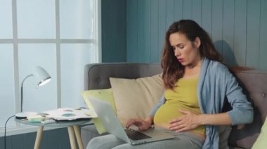 Close up pregnant woman feeling baby movement in her belly indoors.