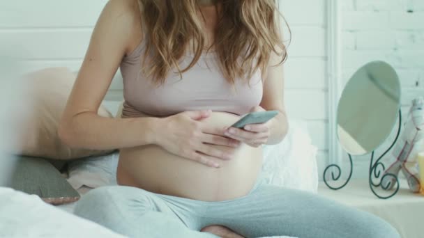 Close up unrecognized belly mother typing message on mobile phone in bedroom. — Stok video