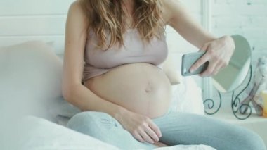 Unrecognized pregnant woman taking selfie of her belly in bed.