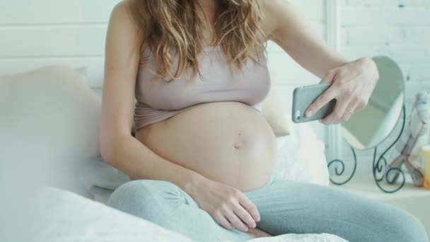 Mulher grávida não reconhecida tomando selfie de sua barriga na cama . — Vídeo de Stock