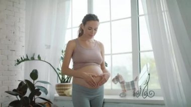 Closeup joyful pregnant woman making heart hand on naked belly at home.