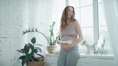 Modern evde kulaklıkla müzik dinleyen gülümseyen hamile kadın..