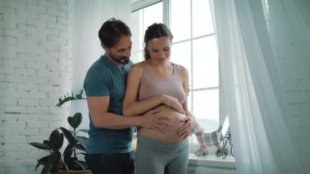 Marido feliz segurando barriga og esposa grávida em casa. Abraço de casal grávida — Vídeo de Stock