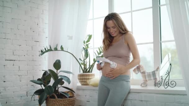 Close up alegre mãe grávida colocando fone de ouvido na barriga em casa . — Vídeo de Stock