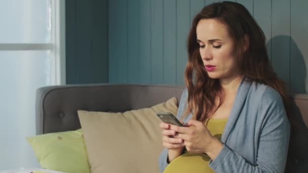 Portrait de femme enceinte concentrée bavardant sur smartphone à la maison . — Video