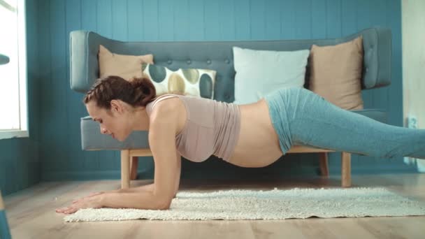 Närbild gravid mage mor utövar yoga planka pose i ljust vardagsrum. — Stockvideo