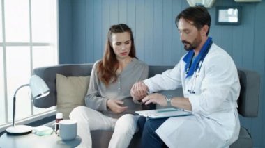 Erkek doktor hamile kadının elinin nabzını bileğiyle kontrol ediyor..