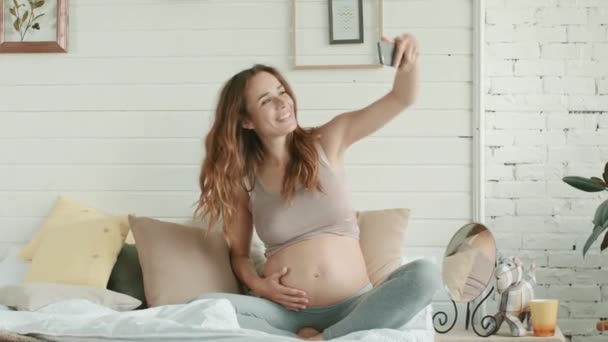 Primeros planos mujer embarazada haciendo selfie teléfono de vientre embarazada en el dormitorio — Vídeos de Stock
