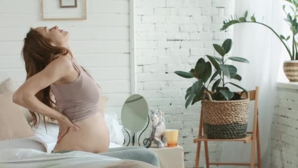 Gravid kvinna sträcker kroppen i sovrummet. Närbild gravid sittande säng hemma — Stockvideo