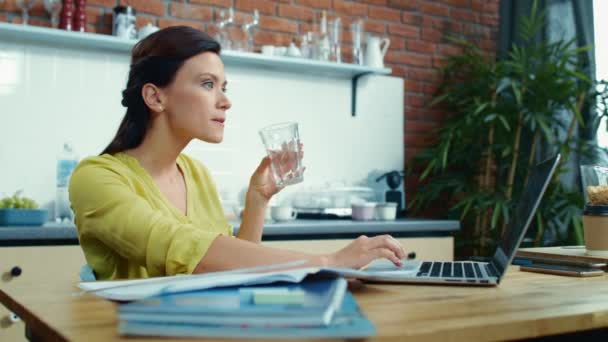 노트북에서 좋은 소식을 읽는 흥분 된 여성. 부엌에서 물을 마시는 소녀. — 비디오