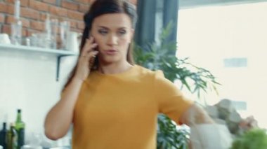Mutfakta telefonla konuşan odaklanmış bir kadın. Evdeki alışveriş çantalarını açan kız..