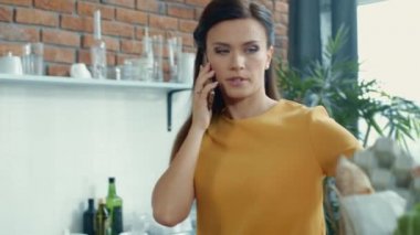Mutfakta alışveriş çantalarını açan bir kadın. Evde telefonla konuşan endişeli kız..