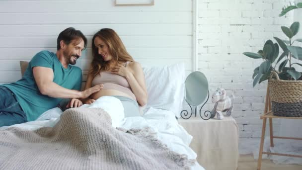 Smiling husband stroking pregnant belly of wife. Pregnant couple huggins in bed — 비디오