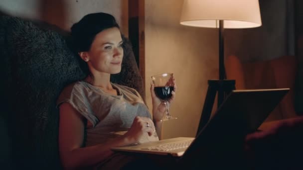 Vrouw die rode wijn drinkt met notitieboekje. Meisje op zoek laptop met wijnglas. — Stockvideo