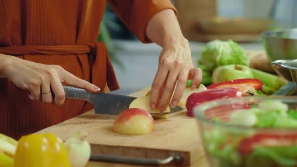 Vrouwelijke handen snijden rode appel op keukenbureau. Meisje proeft gesneden appel thuis — Stockvideo